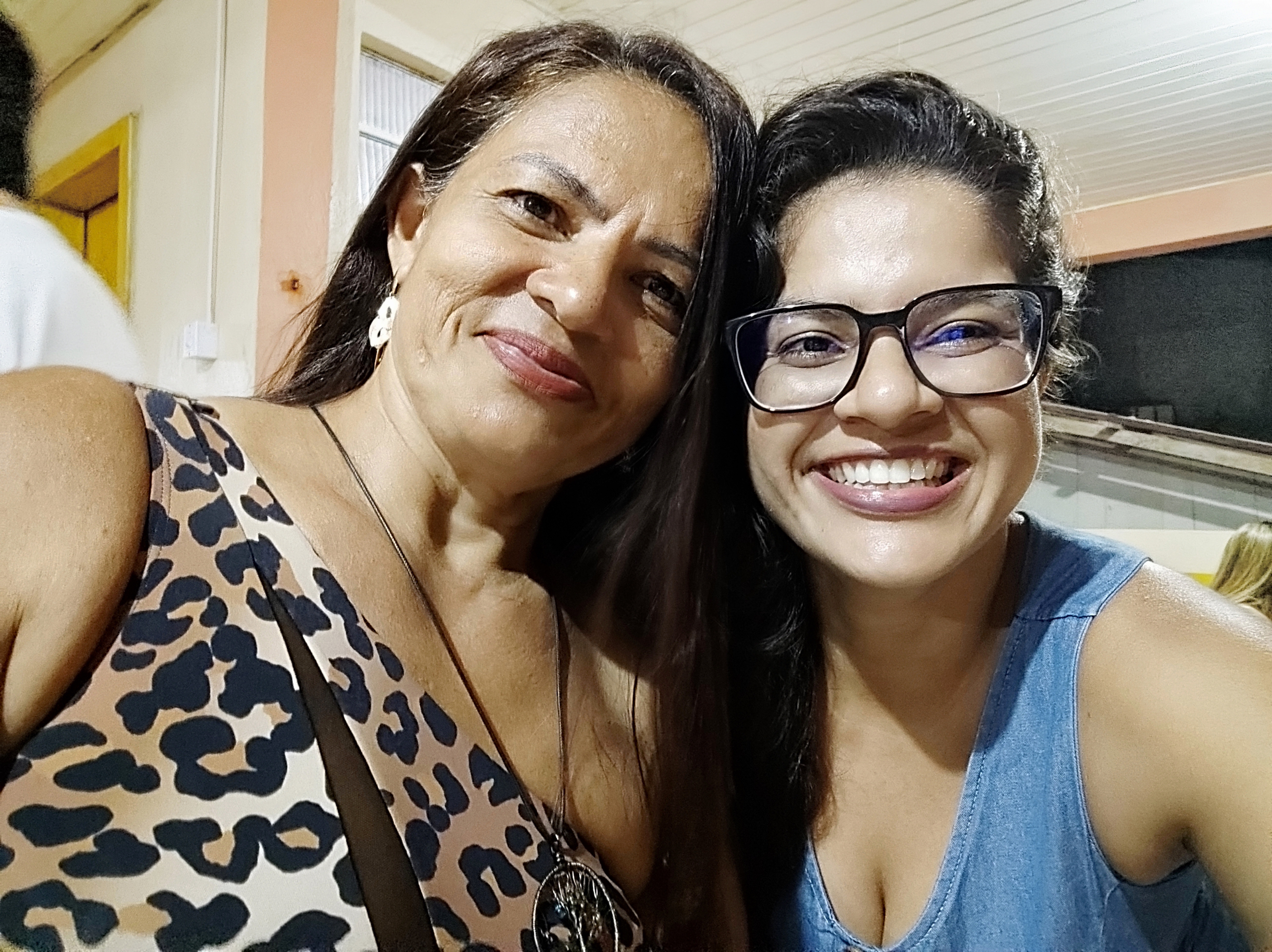 A imagem mostra duas mulheres lado a lado sorrindo. A direta uma jovem e a esquerda uma mulher de meia idade.